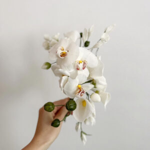 Fehér cukorvirág orchidea csokor, zöld bogyókkal és levelekkel.